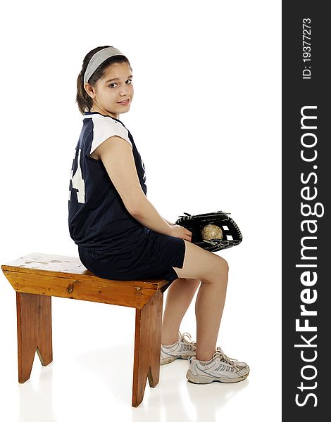 An attractive young teen girl waiting on the bench in her middle school softball uniform. Isolated on white.