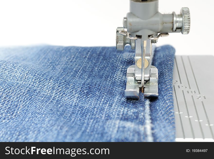 The foot of a sewing machine sewing jeans fabric. The foot of a sewing machine sewing jeans fabric