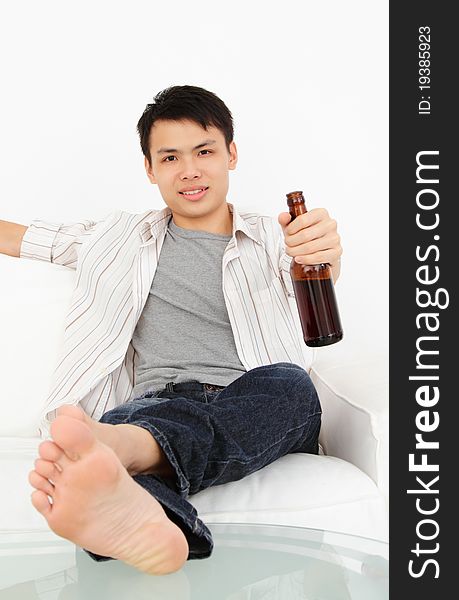 An Asian man watching TV with a bottle of beer with legs up on the table. An Asian man watching TV with a bottle of beer with legs up on the table