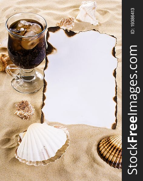 Burned paper on the sand with shells and ice cold drink. Burned paper on the sand with shells and ice cold drink