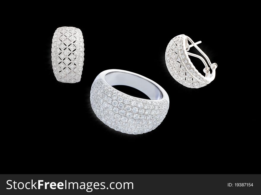 Set of two earrings and ring from white gold with plenty of brilliants on isolated black background. Set of two earrings and ring from white gold with plenty of brilliants on isolated black background