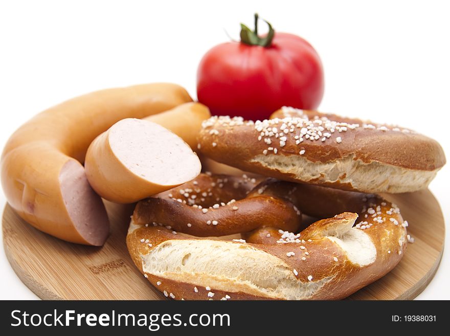 Meat sausage with salt pretzel and tomato onto wood plates