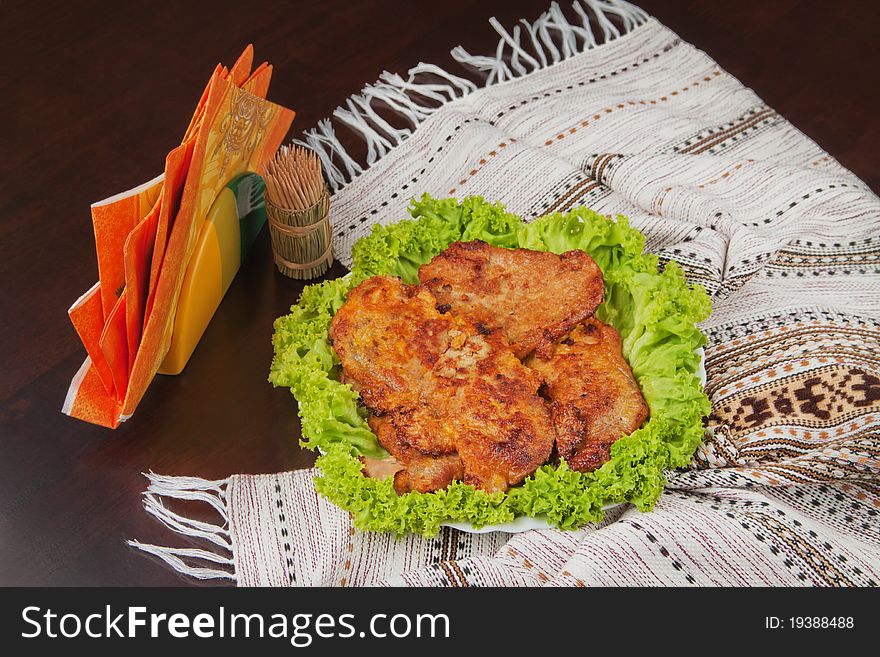There are cutlets on the plate decorated with lettuce, napkins and wooden sticks on the dark brown table with cover.