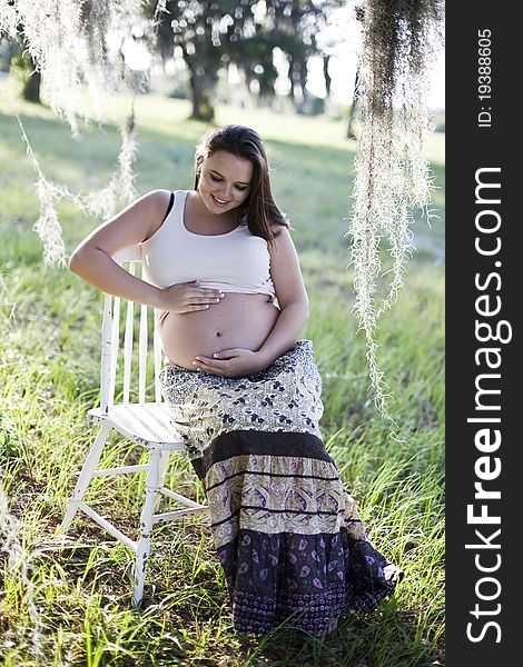 Pregnant woman sitting outside touching and looking at her bare belly.