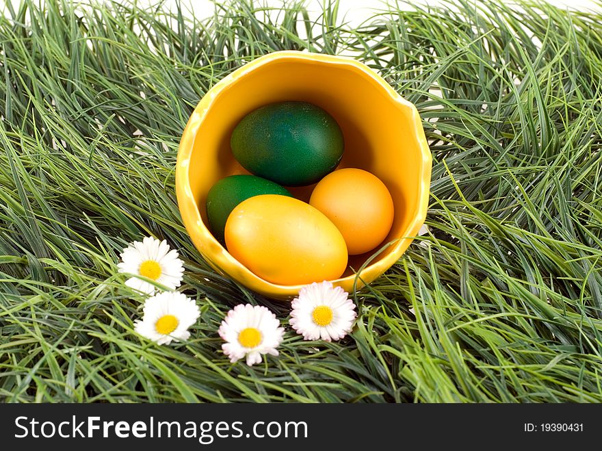Yellow and green eggs in the big eggshell, placed with daisies on a green grass. Studio shot. Yellow and green eggs in the big eggshell, placed with daisies on a green grass. Studio shot.