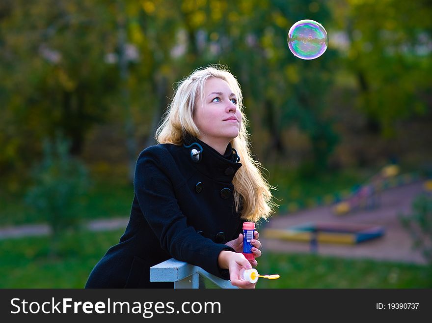 A teenage girl blow bubbles, a large multi-colored bubble flies high and she looks at him. A teenage girl blow bubbles, a large multi-colored bubble flies high and she looks at him