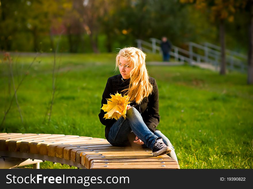 Teenage girl with long blond hair looking at a bouquet of yellow autumn leaves. Teenage girl with long blond hair looking at a bouquet of yellow autumn leaves