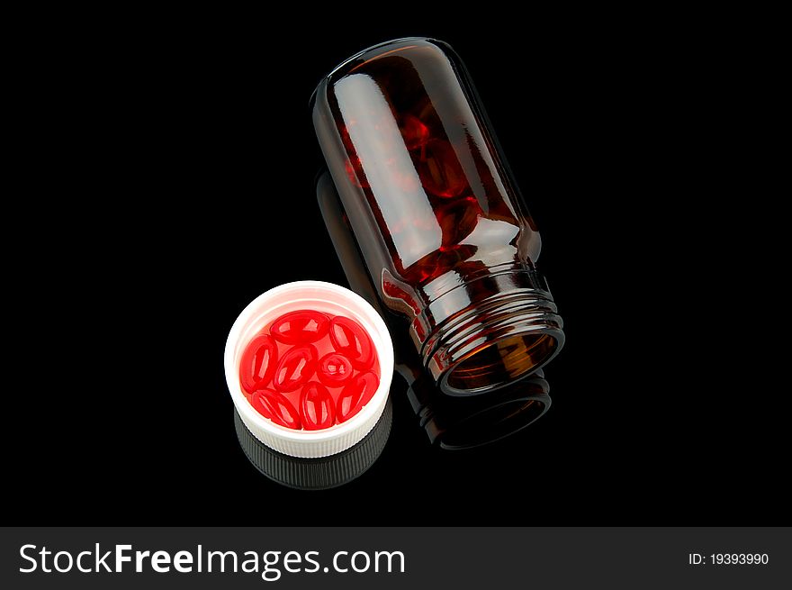 Red vitamin pills in vial on glossy black background