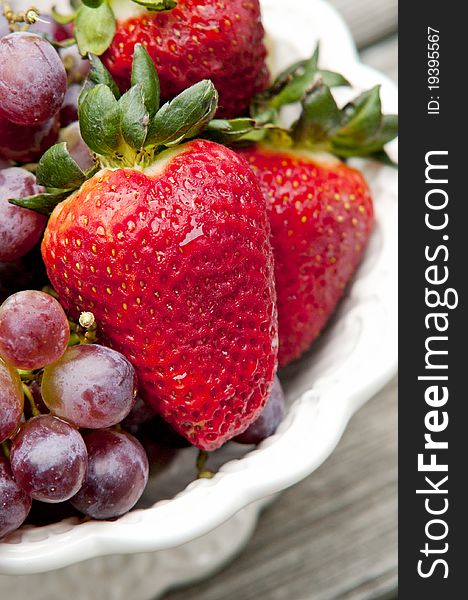 A bowl of fresh strawberries and red grapes with a wooden background, natural light. A bowl of fresh strawberries and red grapes with a wooden background, natural light