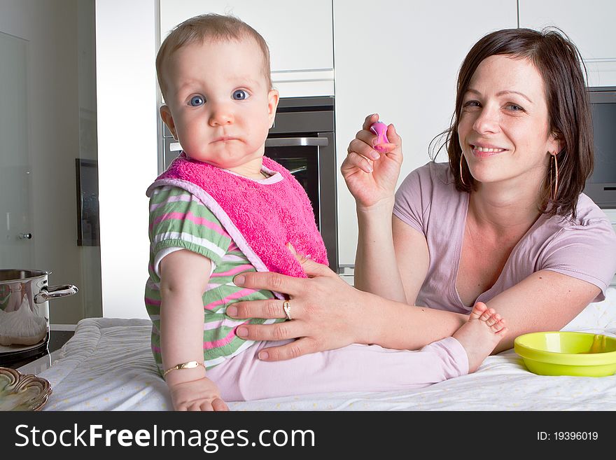 Young mother is feeding her baby in a modern kitchen setting. Young mother is feeding her baby in a modern kitchen setting.