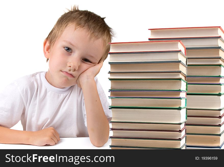 Tired schoolboy sits at the table with piles of books