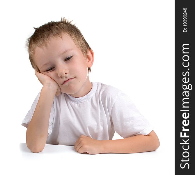 Sad boy sits at the table on a white background