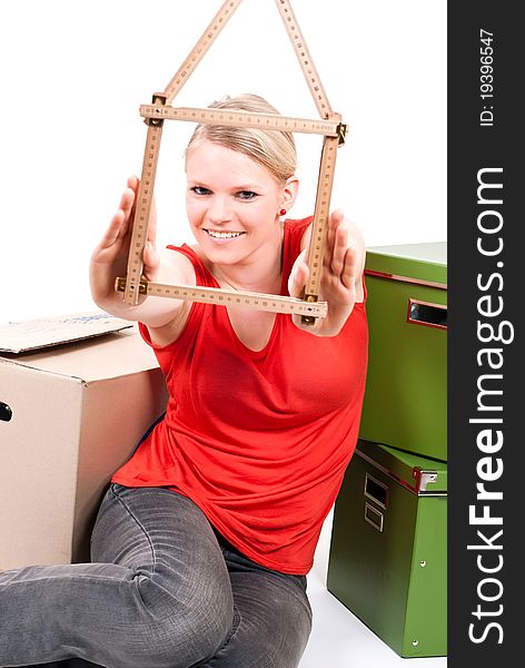 Young woman with a folding rule as a house symbol sits between move cardboards. Young woman with a folding rule as a house symbol sits between move cardboards