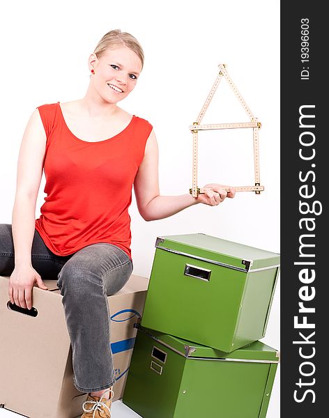 A young woman with a folding rule as a house symbol sits on moving box. A young woman with a folding rule as a house symbol sits on moving box