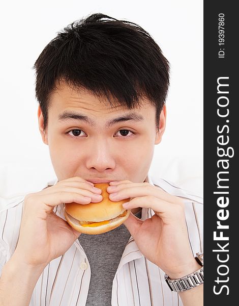 A hungry young Asian man biting into a burger against white background. A hungry young Asian man biting into a burger against white background