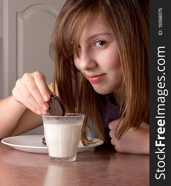 Cute girl looks while dunking a chocolate cookie in milk. Cute girl looks while dunking a chocolate cookie in milk