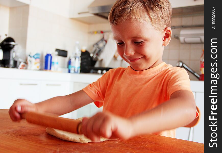 Blond hair little boy enjoys making pizza in the kitchen