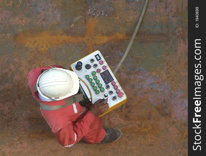 Man wearing a construction worker's helmet with remote control, standing on a rusty steel deck. Man wearing a construction worker's helmet with remote control, standing on a rusty steel deck.