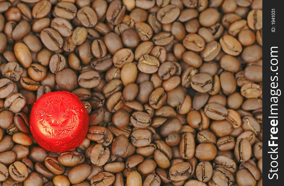 A piece of red chocolate on a stack of coffee beans. Selective focus on the chocolate, the beans are blurred. A piece of red chocolate on a stack of coffee beans. Selective focus on the chocolate, the beans are blurred.