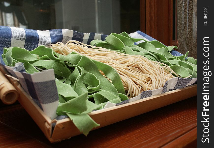 White and green spaghetti in the wooden plate on the table