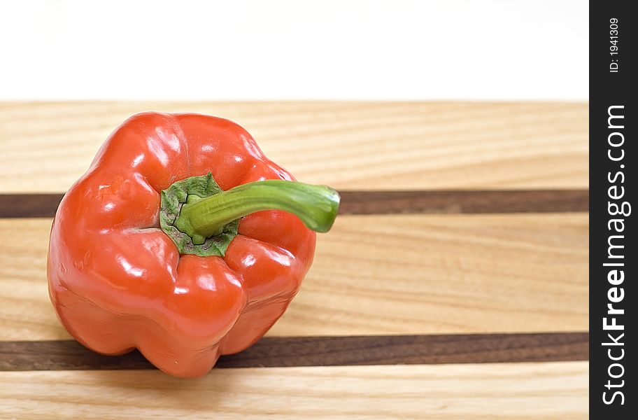 A red bell pepper on a wooden cutting board - room on right for text. A red bell pepper on a wooden cutting board - room on right for text.