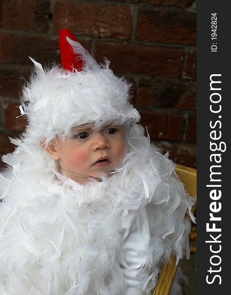 Image of baby wearing a chicken costume, sitting on a chair. Image of baby wearing a chicken costume, sitting on a chair