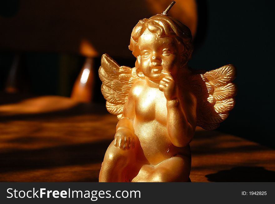 A golden cherub candle glows in the sunlight.