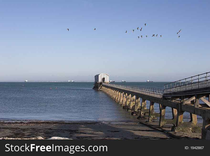 Lifeboat station out to sea with flock of birds in flight. Lifeboat station out to sea with flock of birds in flight