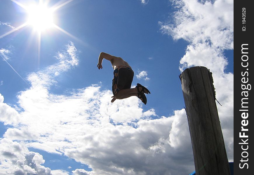 Man jumps off piling under sun and blue sky. Man jumps off piling under sun and blue sky.