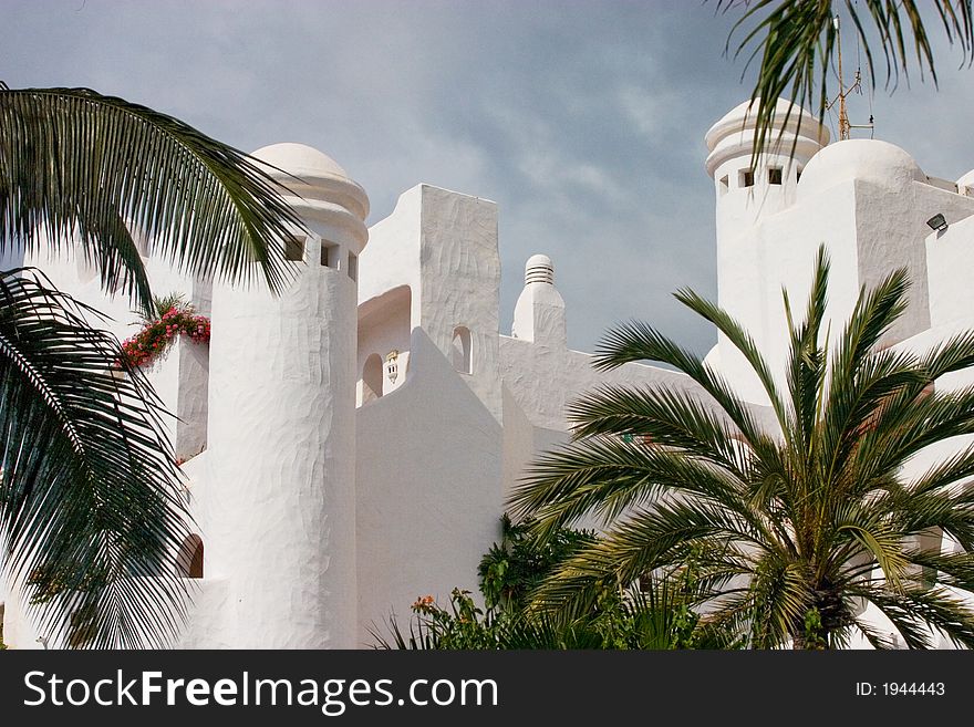 There is white building between palms against a background of the sky. There is white building between palms against a background of the sky