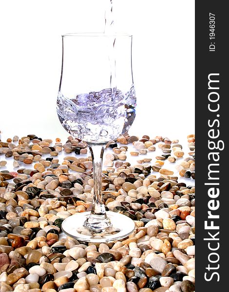 Water poured into a wine glass set on polished stones, isolated on white