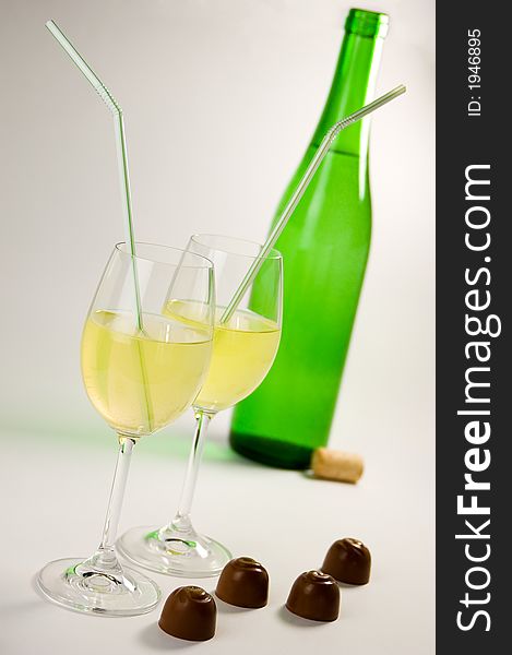 Green bottle, two glasses with yelllow liquid and straws, four chocolates. Green bottle, two glasses with yelllow liquid and straws, four chocolates.