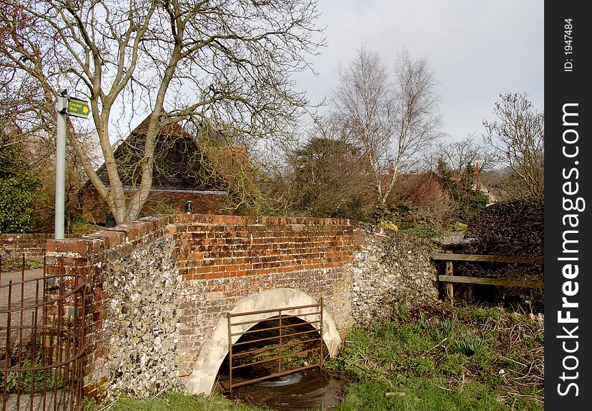 Quaint Brick and Flint Road Bridge over an English Village Stream with a footpath sign. Quaint Brick and Flint Road Bridge over an English Village Stream with a footpath sign.