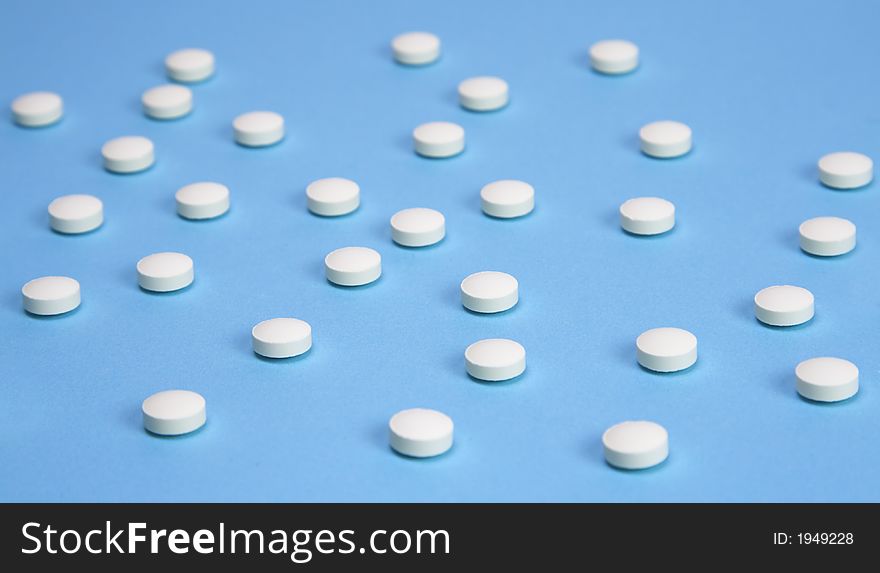 A medical background with white pills over a blue background. Selective focus on the middle pills. A medical background with white pills over a blue background. Selective focus on the middle pills.