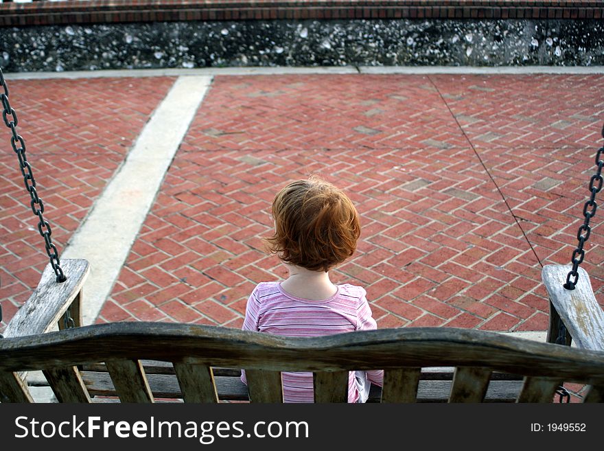 Little girl with red hair sitting on a park swing. Little girl with red hair sitting on a park swing.