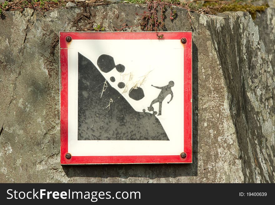 A square sign with red border showing the potential danger of falling rocks, fixed onto a wall with rusty screws. A square sign with red border showing the potential danger of falling rocks, fixed onto a wall with rusty screws.