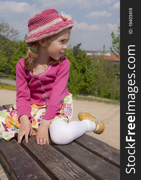 Little girl dressed in pink is sitting outdoor. Little girl dressed in pink is sitting outdoor.