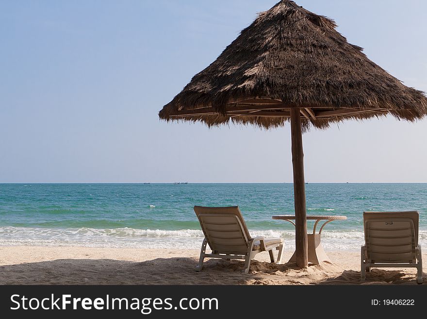 Straw umbrella and two chaise lounges on an empty sea beach. Straw umbrella and two chaise lounges on an empty sea beach