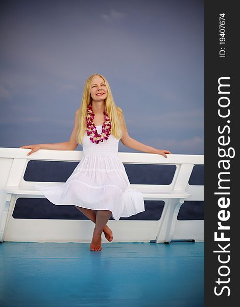 Beautiful smiling blonde woman wearing white dress and Thai flower beads sitting on white bench on ship. Beautiful smiling blonde woman wearing white dress and Thai flower beads sitting on white bench on ship.