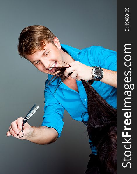 Portrait of young man hairdresser working with scissors wearing blue shirt on gray background