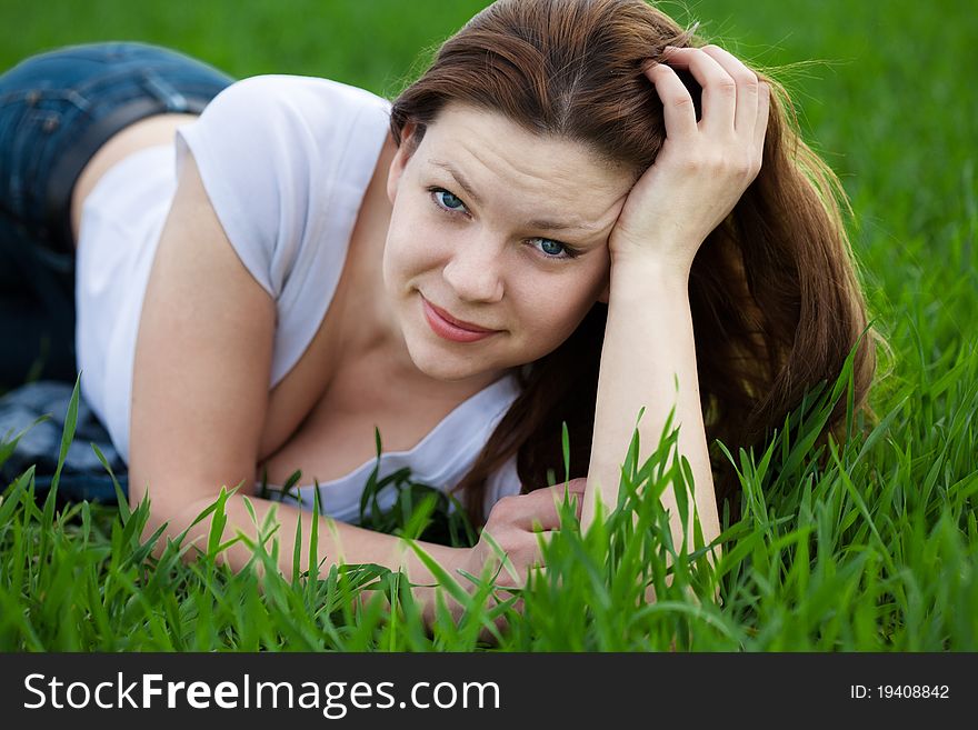 Cute woman dressed in white t-shirt and jeans lying in the grass in summer. Cute woman dressed in white t-shirt and jeans lying in the grass in summer