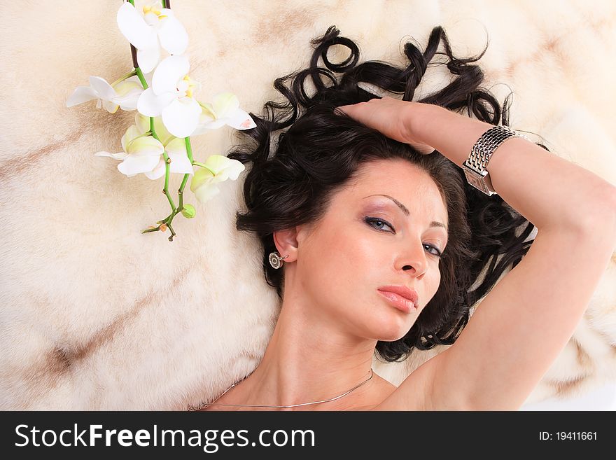 Young beautiful woman with flower lies on fur coat