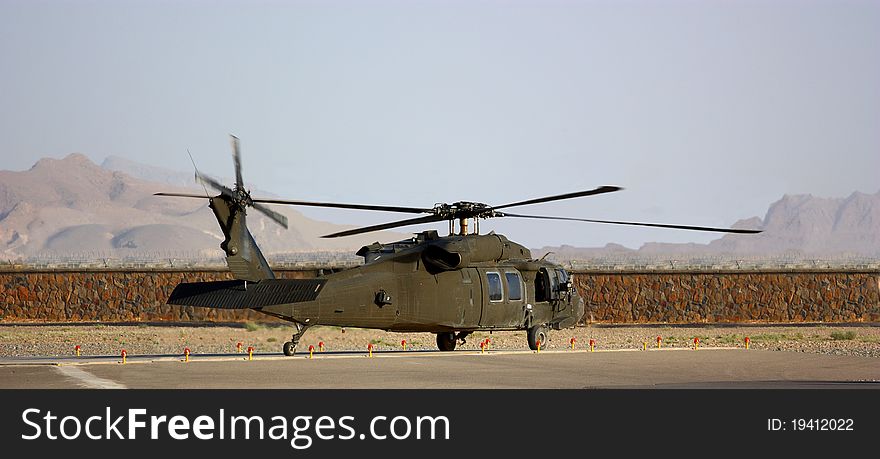 A military helicopter (Black Hawk) on helipad outdoor behind a stone wall, mountains and clear sky. A military helicopter (Black Hawk) on helipad outdoor behind a stone wall, mountains and clear sky