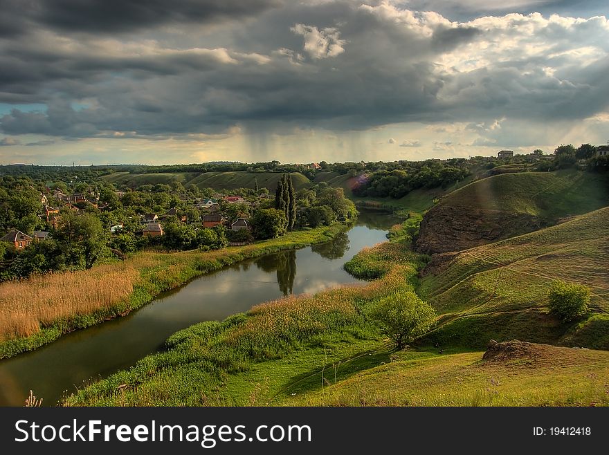 Small black river between green-yellow hills with stormy clouds. Small black river between green-yellow hills with stormy clouds