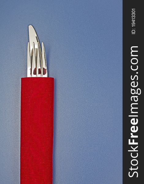 Knife and fork on red napkin on blue table. Knife and fork on red napkin on blue table
