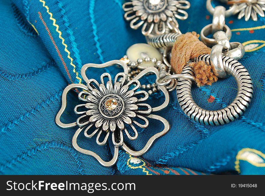 Silver necklace with flowers on the blue fabric  in East style background. Silver necklace with flowers on the blue fabric  in East style background.