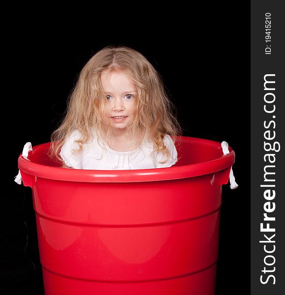 A cute girl is playing in a red bucket. A cute girl is playing in a red bucket.