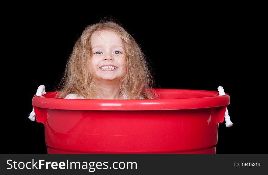 A cute girl is playing in a red bucket. A cute girl is playing in a red bucket.