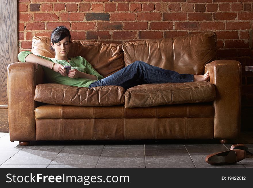 Young woman with phone on sofa lying down