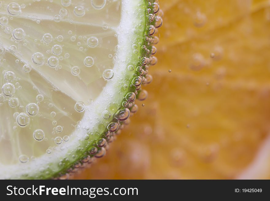 Slice of lime with bubbles on orange background.